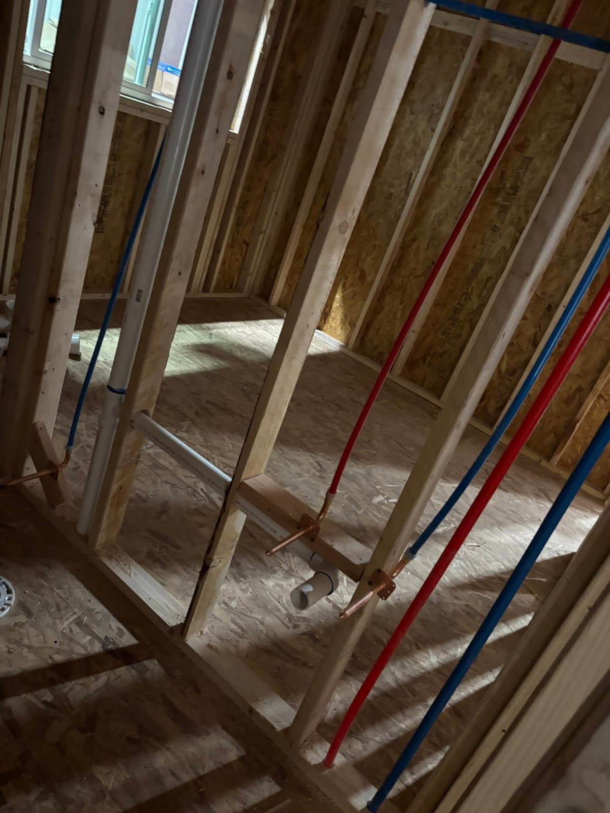 Red and blue PEX plus PVC piping installed in wood framing