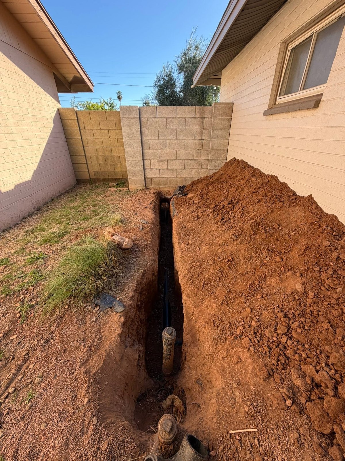 Excavated trench beside a home with installed underground pipe